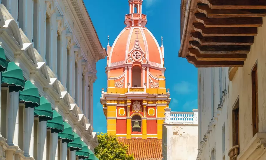Cartagena cathedral's yellow and red bell tower and coral dome, framed by colonial buildings and a Colombian flag