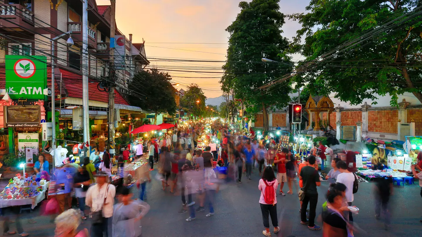 A busy night market running down the centre of one of the main roads in Chiang Mai's old city. A stream of people (blurred to indicate they are in motion) walk alongside the stalls.