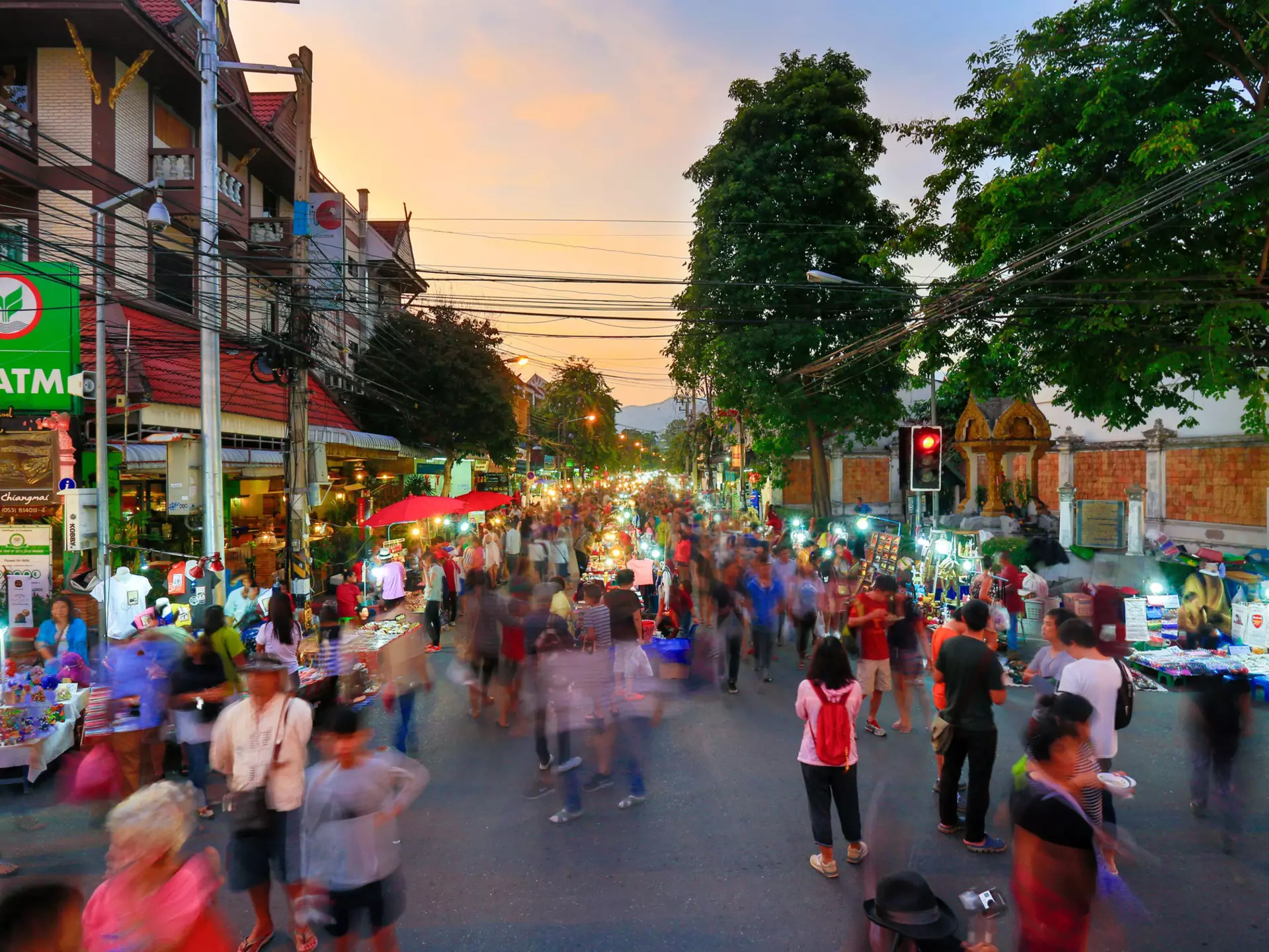 A busy night market running down the centre of one of the main roads in Chiang Mai's old city. A stream of people (blurred to indicate they are in motion) walk alongside the stalls.