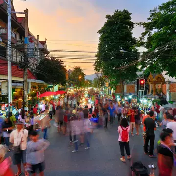 A busy night market running down the centre of one of the main roads in Chiang Mai's old city. A stream of people (blurred to indicate they are in motion) walk alongside the stalls.