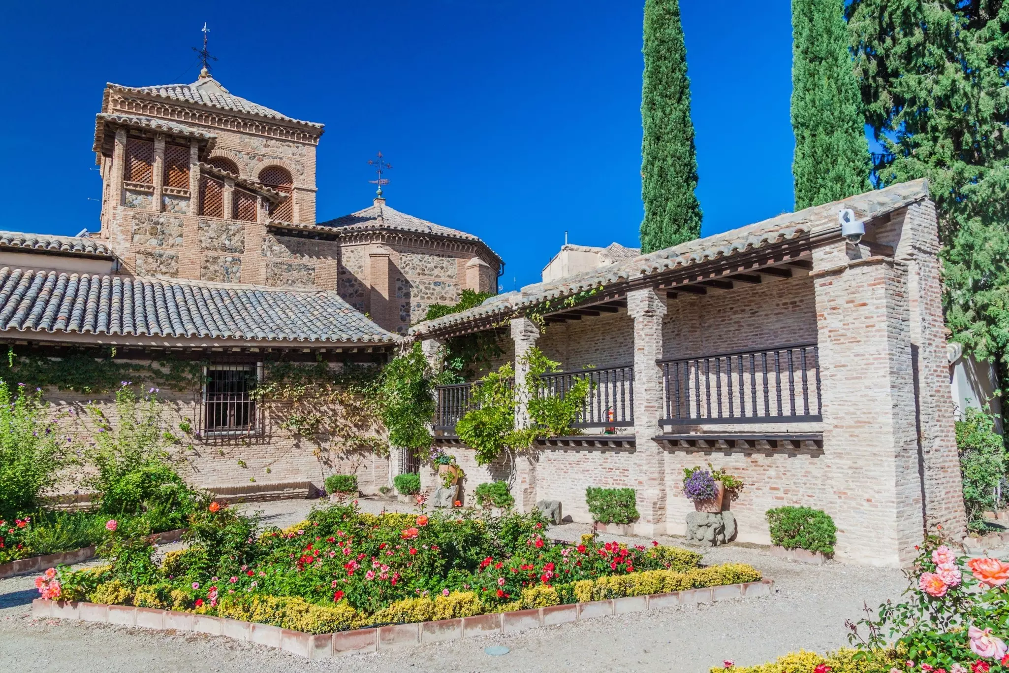 Exterior of a walled, stone house with plants and flowers displayed in its sunny courtyard