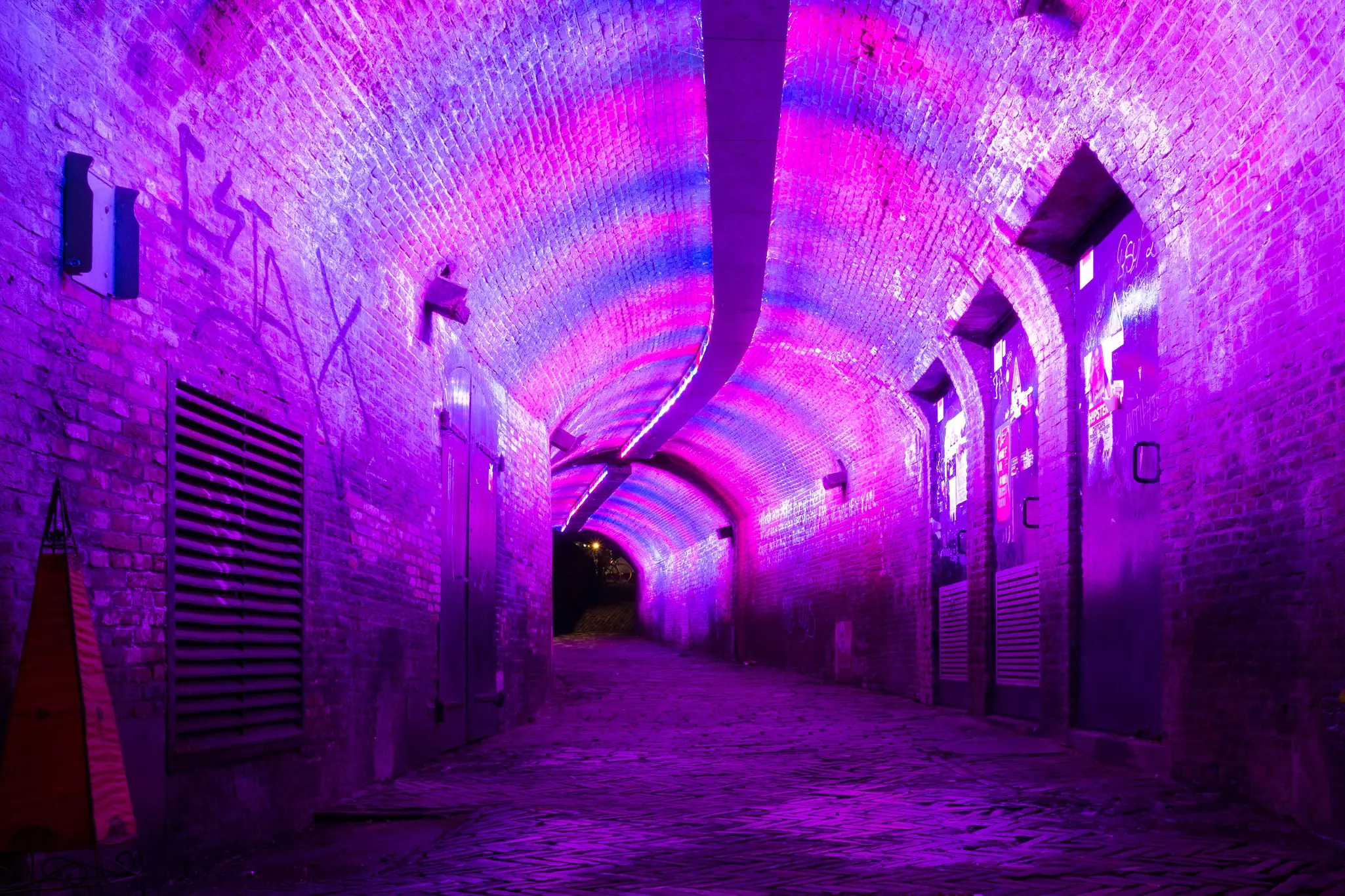 A tunnel with a brick vault is illuminated by pink and purple lights.