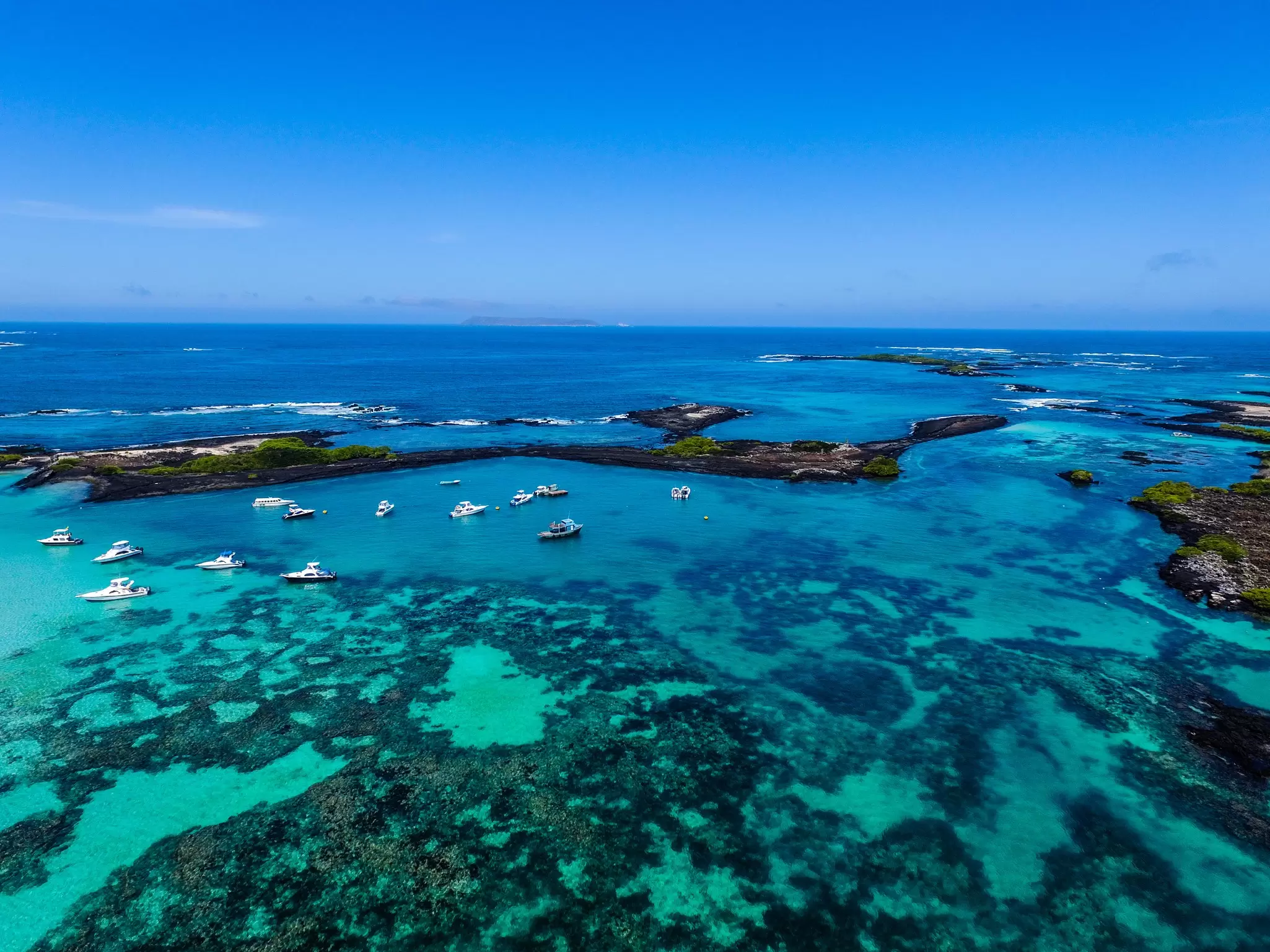 A series of small boats moored in a sheltered harbor with shallow turquoise waters; San Cristóbal, the Galapagos Islands. 