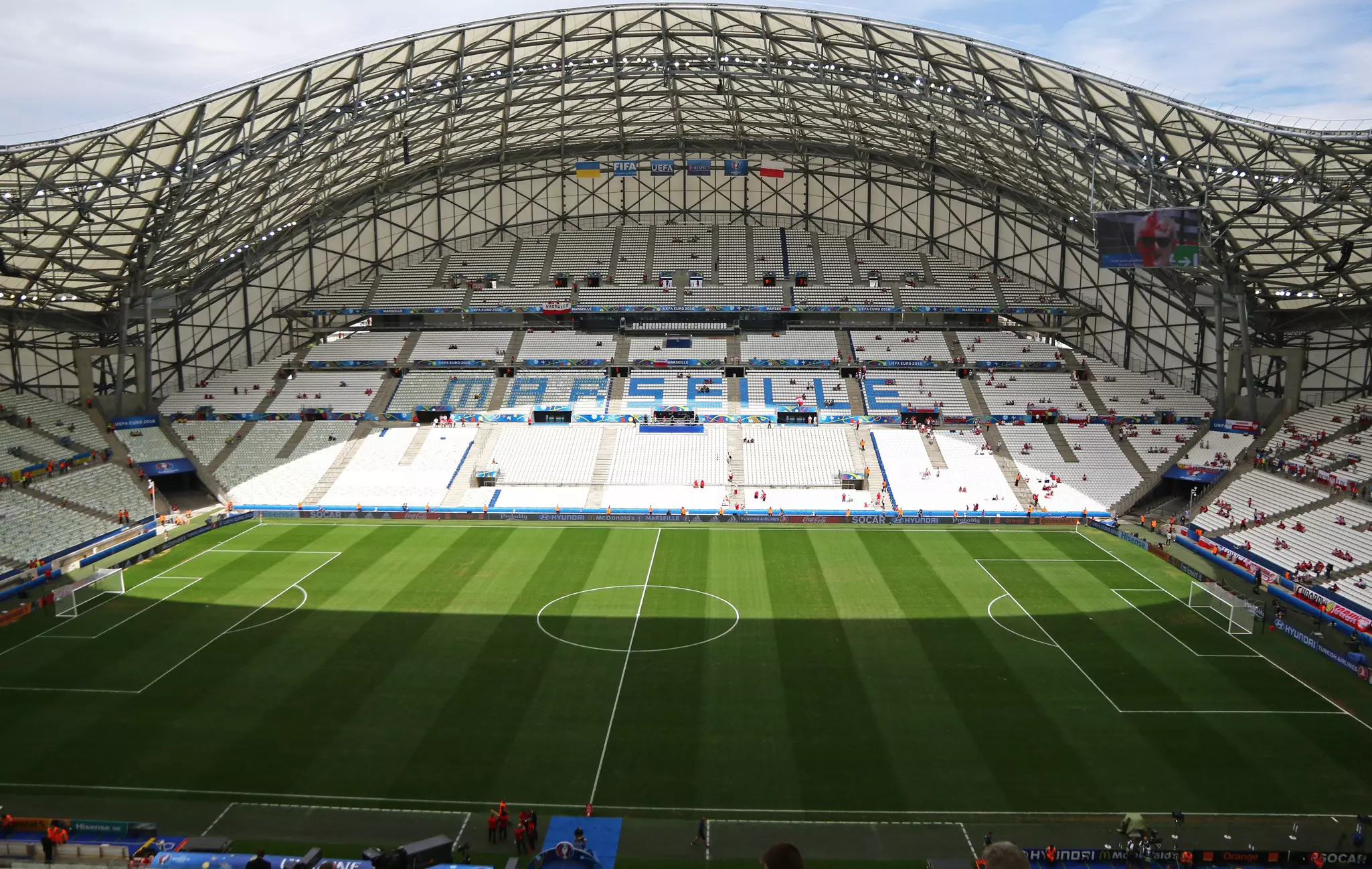A vast sports stadium with a green football pitch and white seats.