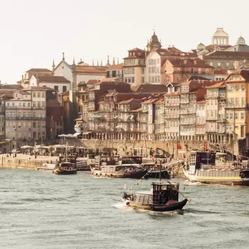 Traditional wooden boats on a river in front of a waterfront of tall, colourful old houses, with church towers above.