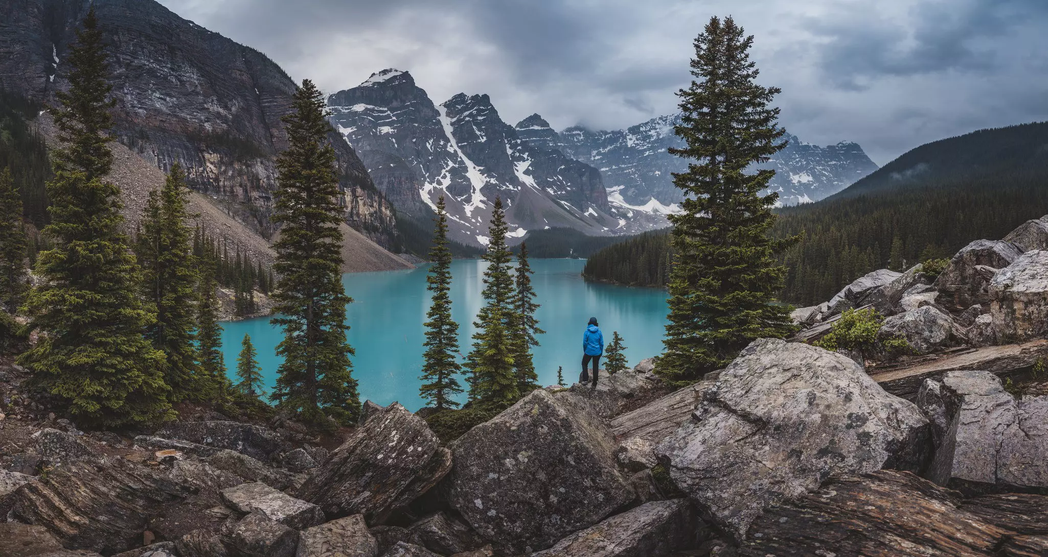 Hiker stands on top of rocks near Moraine Lake with the Canadian Rockies in the background.