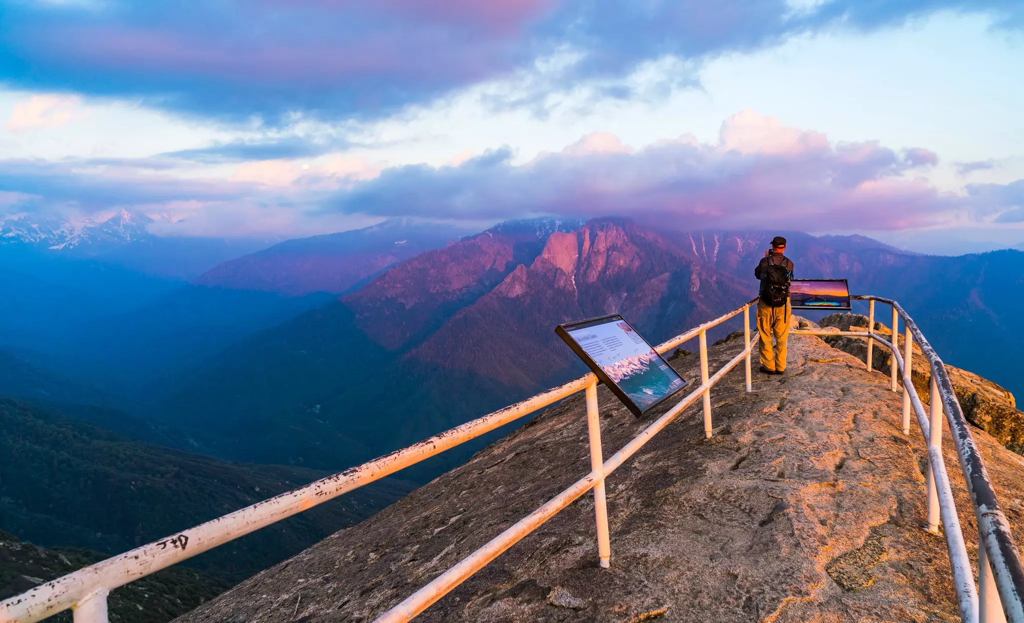 A man takes a picture of the sunset from a lookout