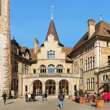 Turreted stone facade of the Landesmuseum in Zürich with visitors walking towards its arched entrance.