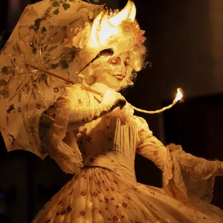 A costumed performer in all white carries a parasol.