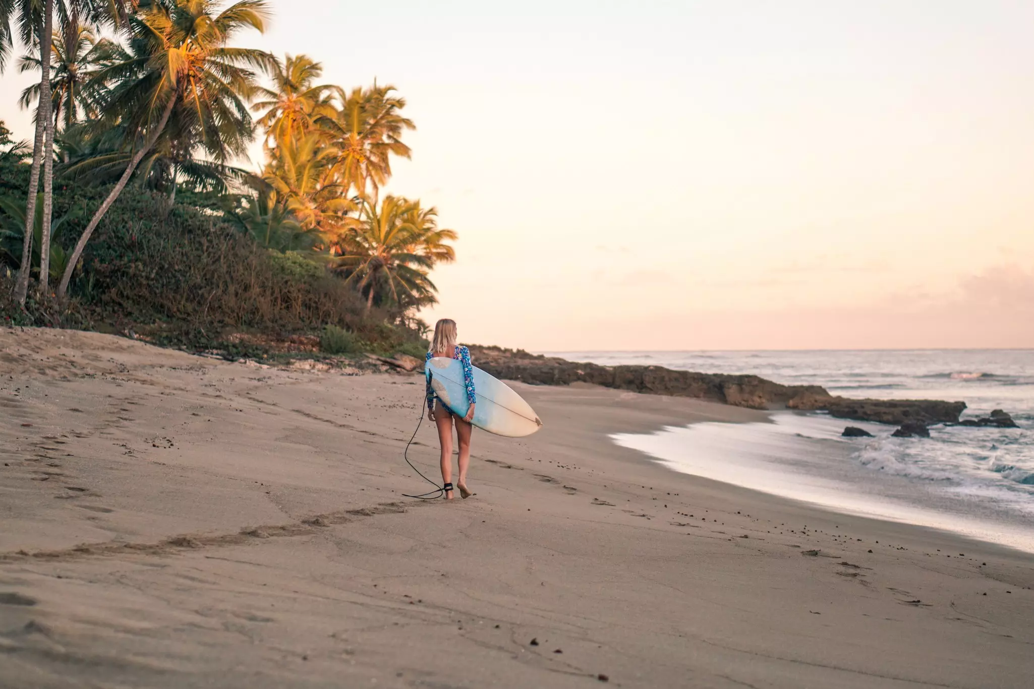 Portrait of blond surfer girl with white surf board in blue ocean pictured from the water in Encuentro beach in Dominican Republic.