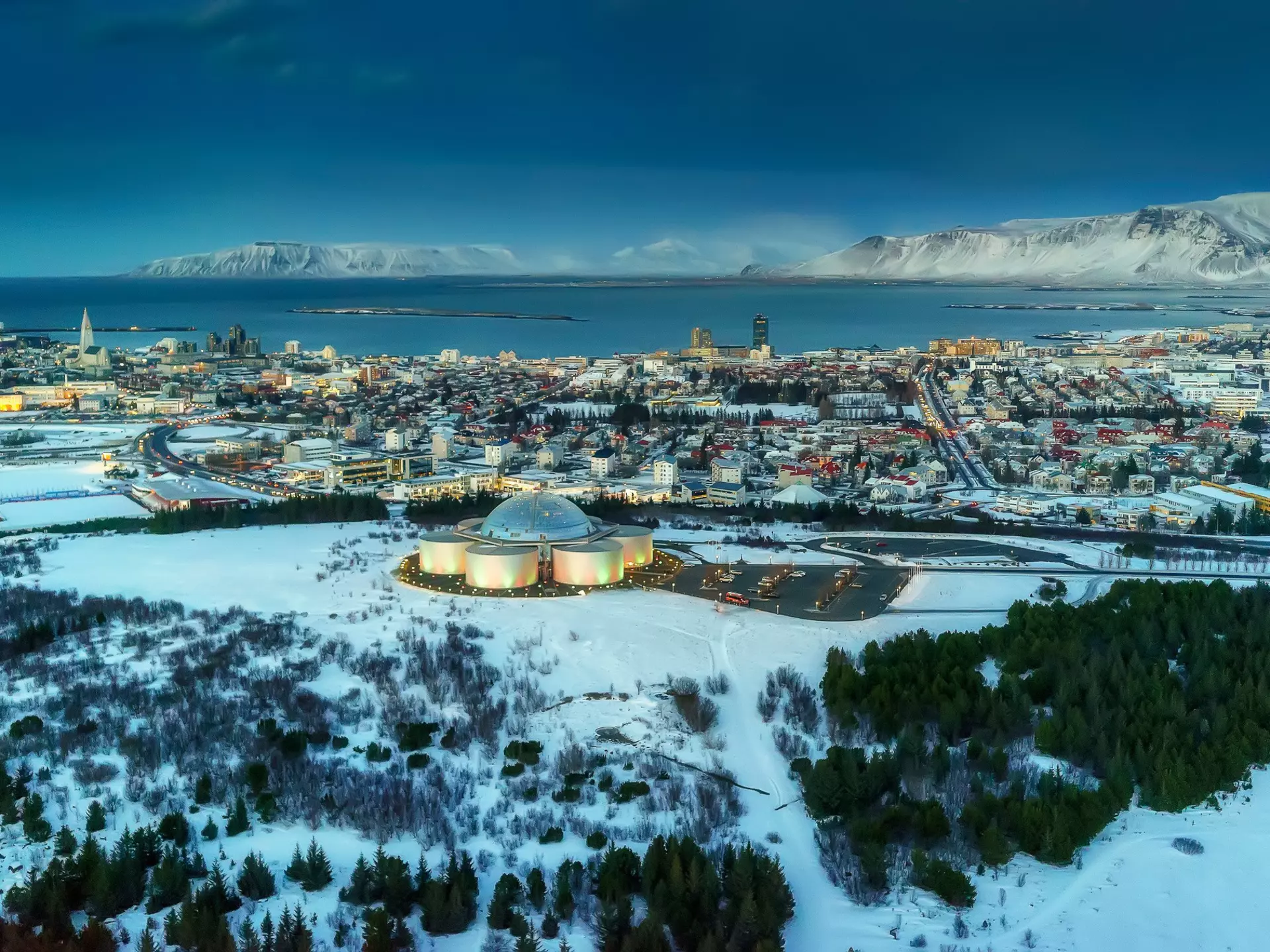 A domed building on a hill at the edge of a small harbor city covered in winter snow.