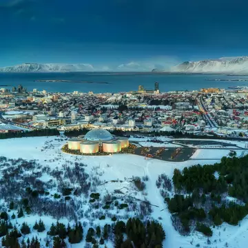 A domed building on a hill at the edge of a small harbor city covered in winter snow.