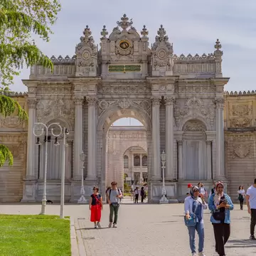 People walk away from an ornate archway at a palace complex.