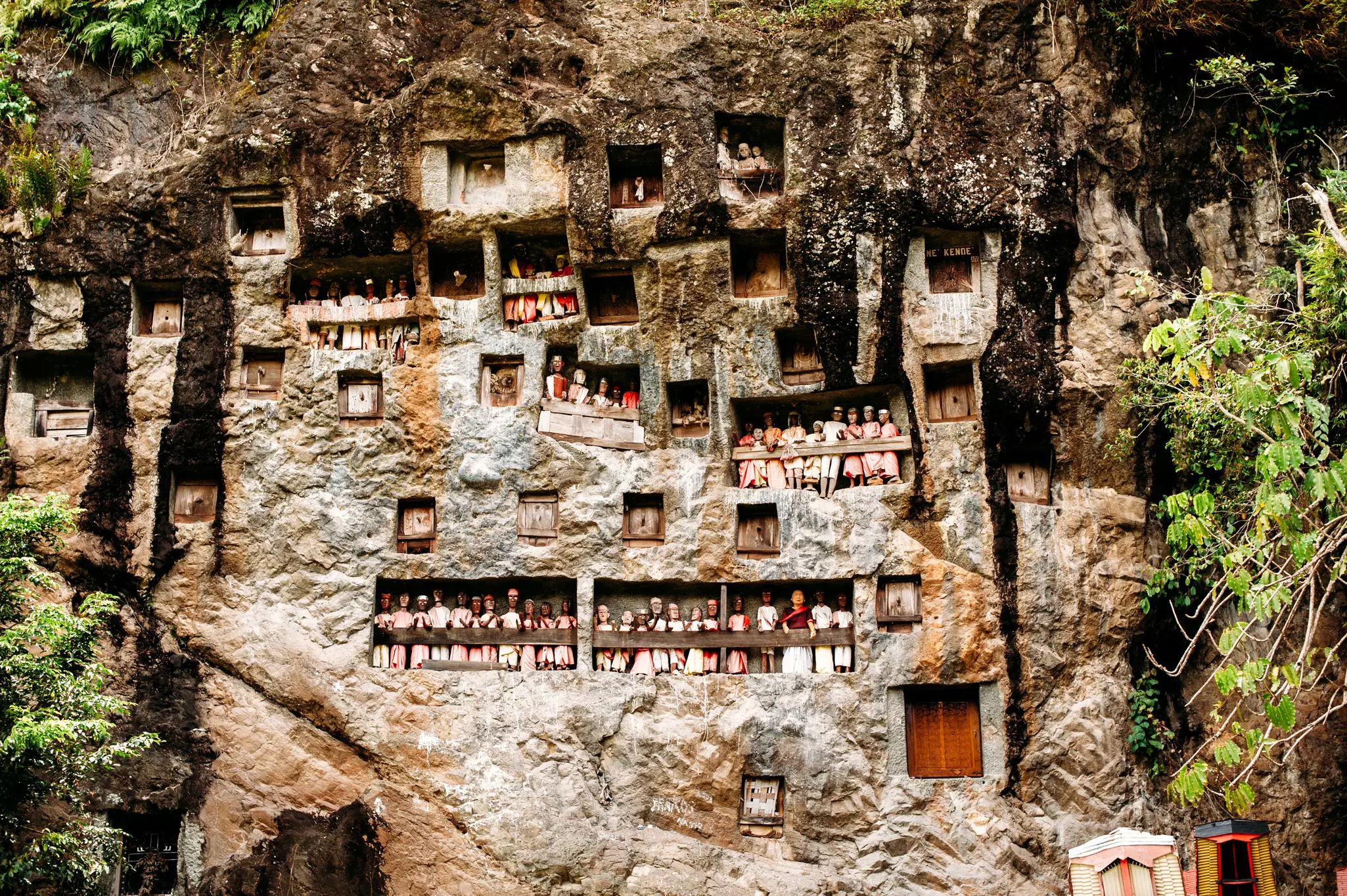 Openings carved into a rock face in Indonesia display wooden statues.