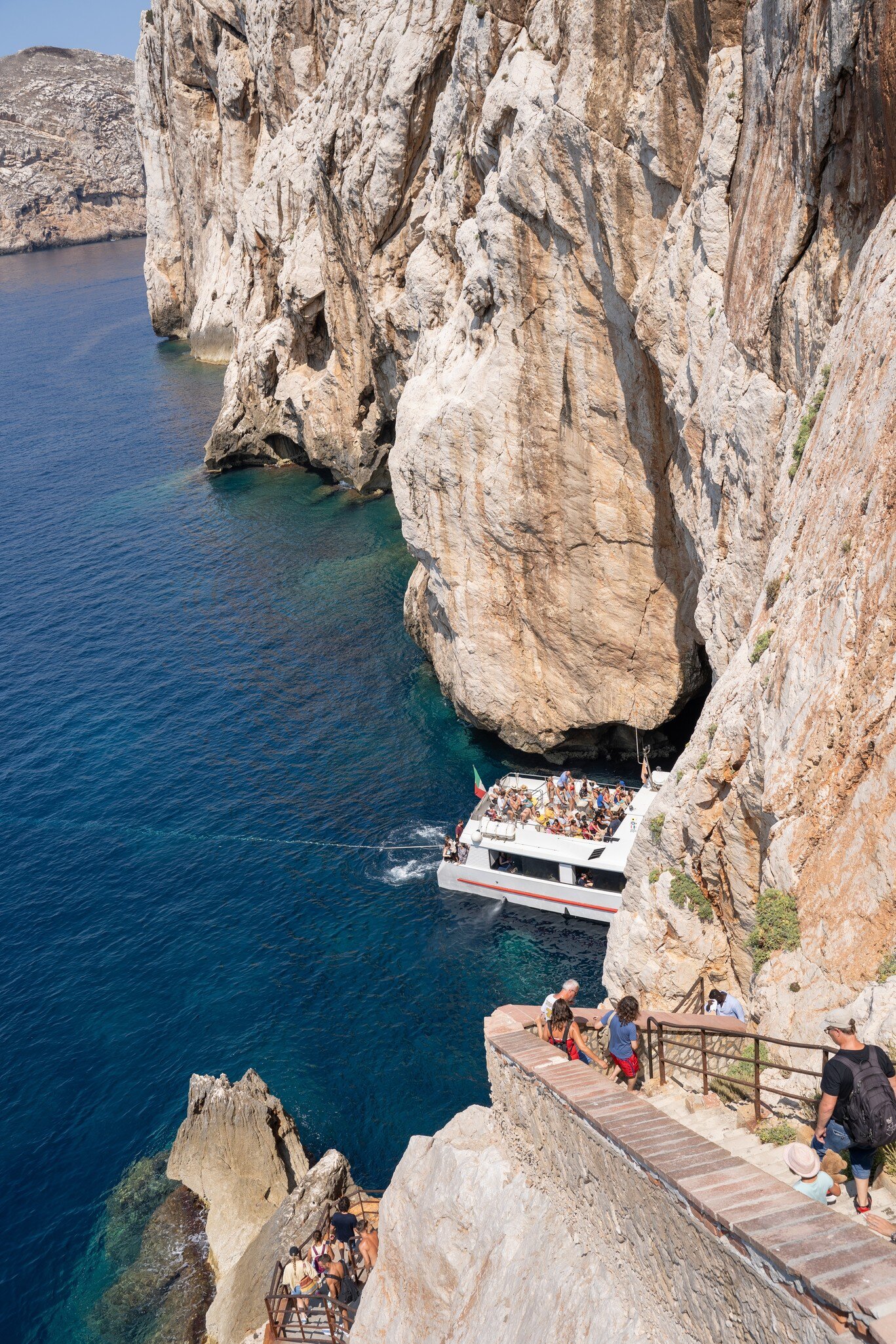 Tourists accessing the Grotto of Neptune (Grotta di Nettuno) on foot via the steep stairs and by boat directly into the cave, located near Alghero.