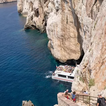 Tourists accessing the Grotto of Neptune (Grotta di Nettuno) on foot via the steep stairs and by boat directly into the cave, located near Alghero.