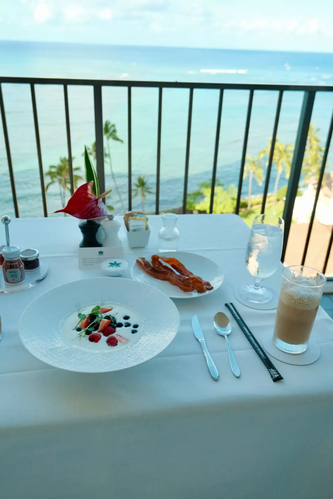 A breakfast of yoghurt, fruit and bacon served on a table on a balcony overlooking the ocean