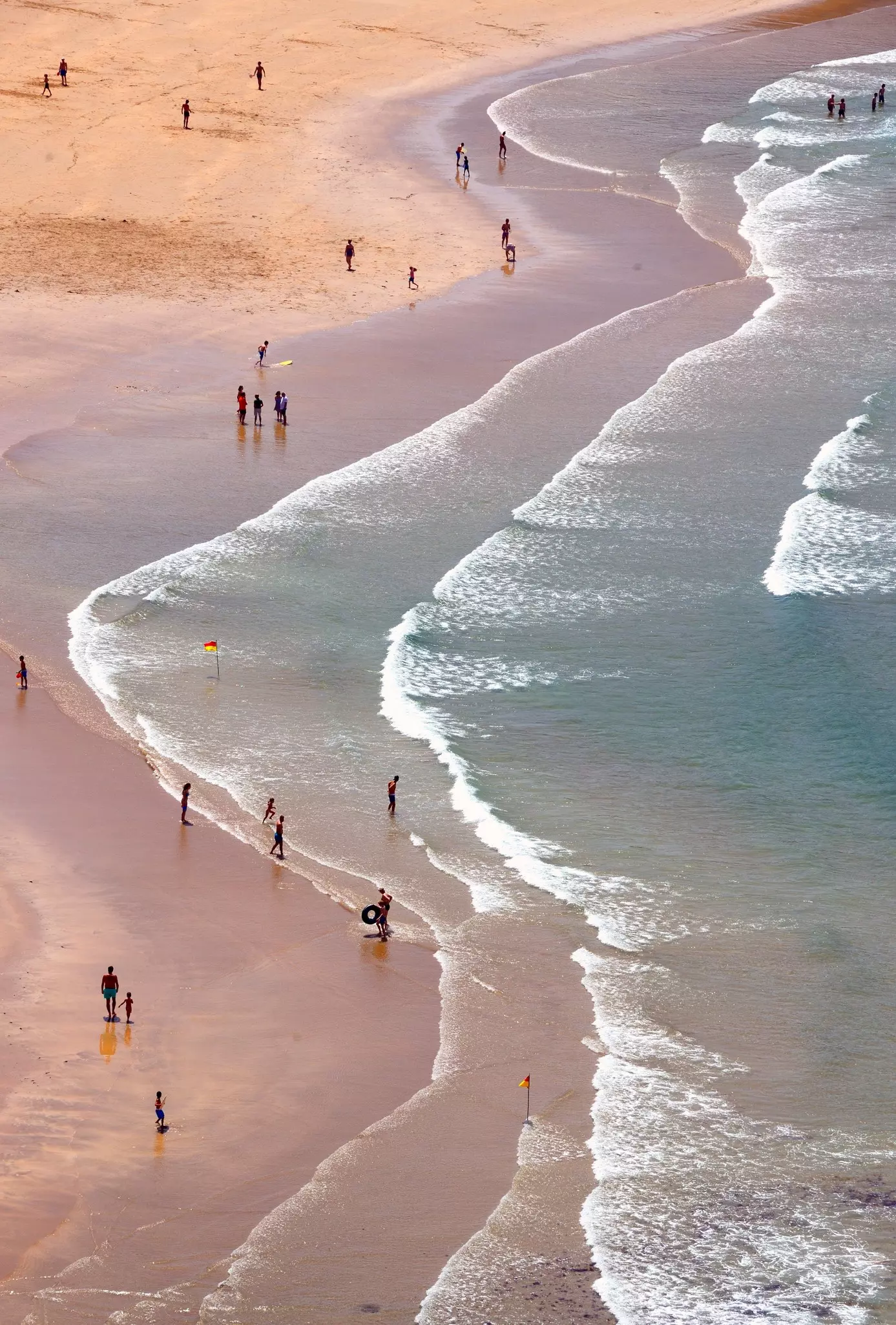People stand in the surf along Arrifana beach, Costa Vicentina, Vicentine Coast Natural Park, view from above.