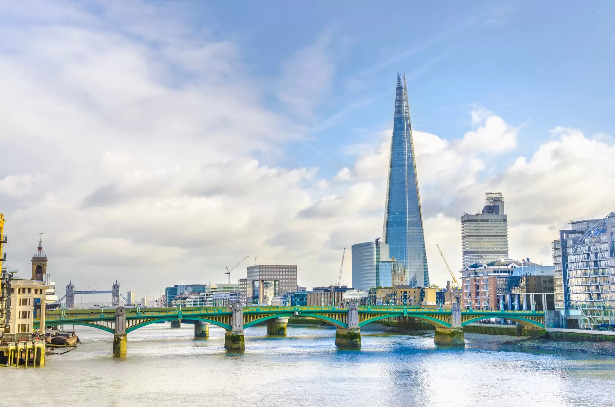 A pointed glass and steel skyscraper stands tall over a river in a city: The Shard, London.