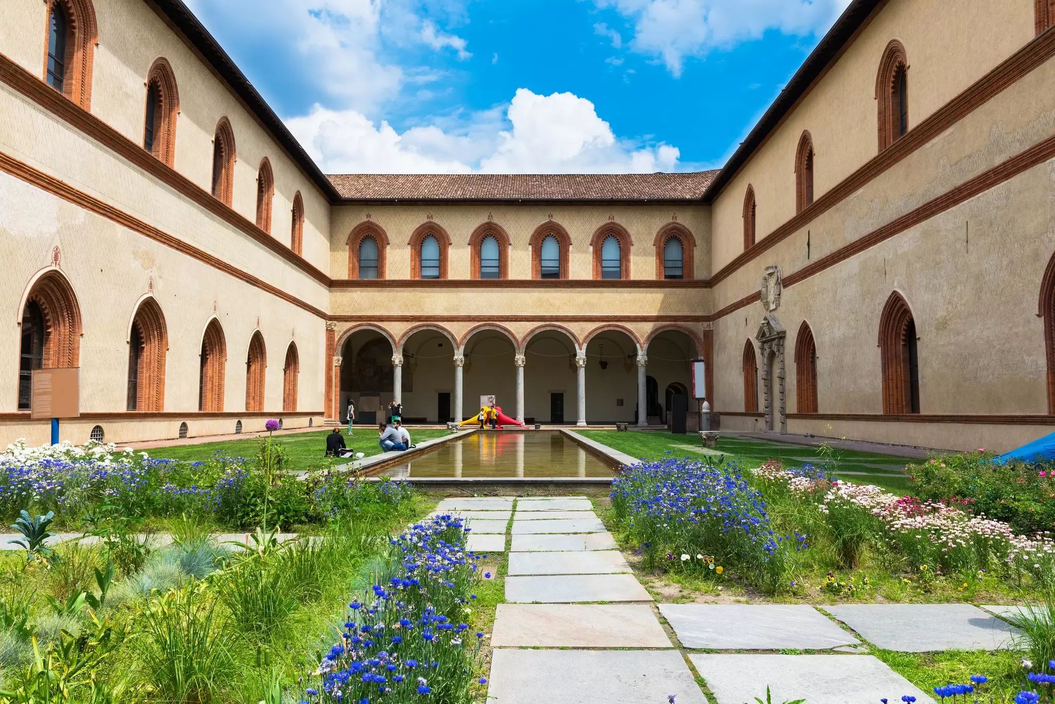 Visitors relax in the courtyard of Sforza Castle on a sunny day in Milan.