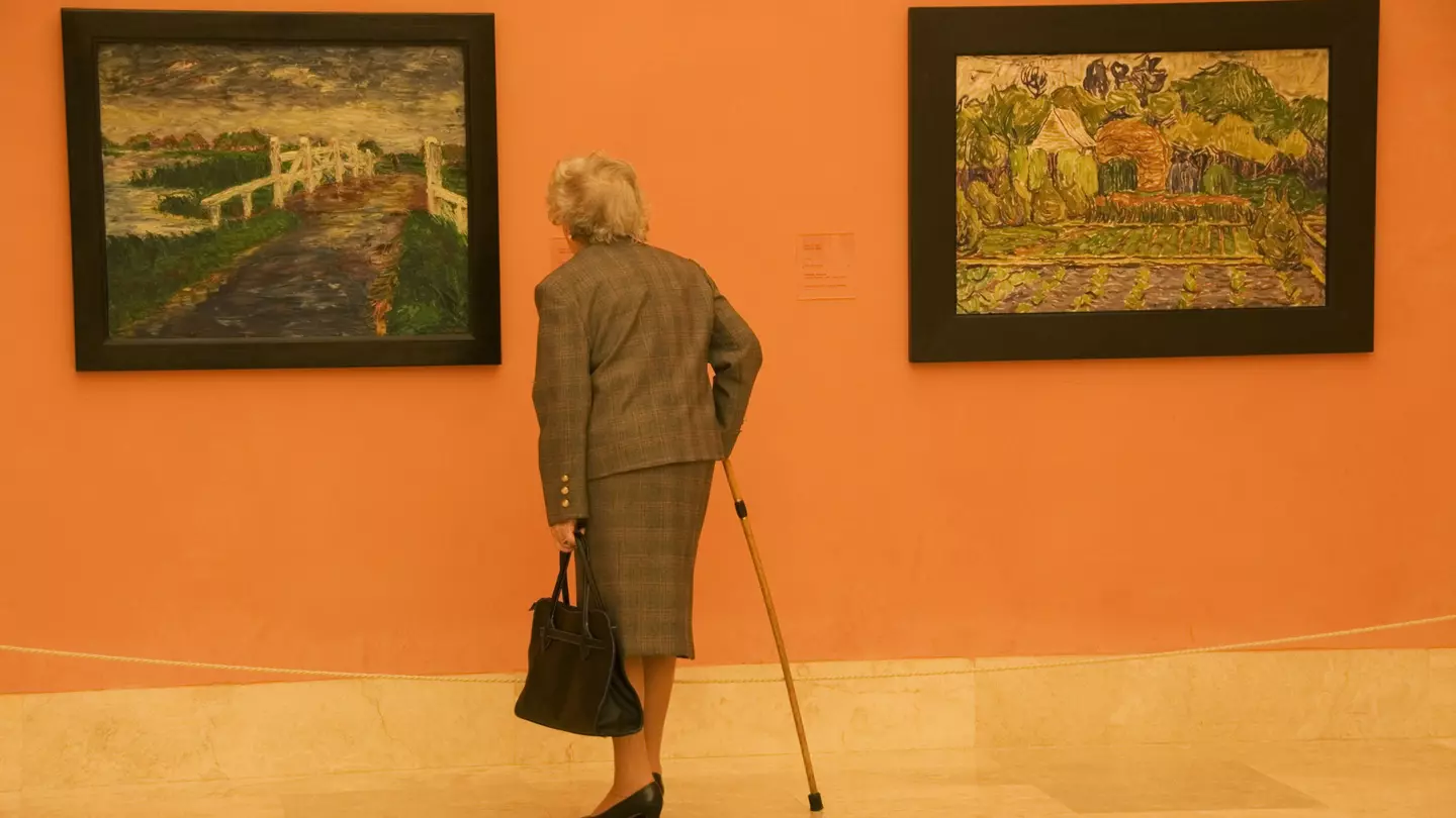 An elderly woman in a suit and with a cane admires two paintings (one by Vincent van Gogh) at Museo Thyssen-Bornemisza, Madrid, Spain