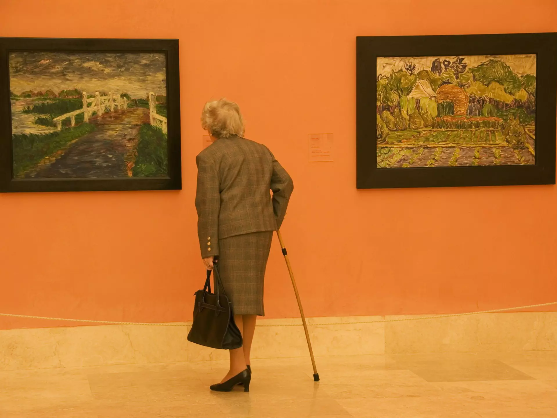 An elderly woman in a suit and with a cane admires two paintings (one by Vincent van Gogh) at Museo Thyssen-Bornemisza, Madrid, Spain