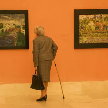 An elderly woman in a suit and with a cane admires two paintings (one by Vincent van Gogh) at Museo Thyssen-Bornemisza, Madrid, Spain