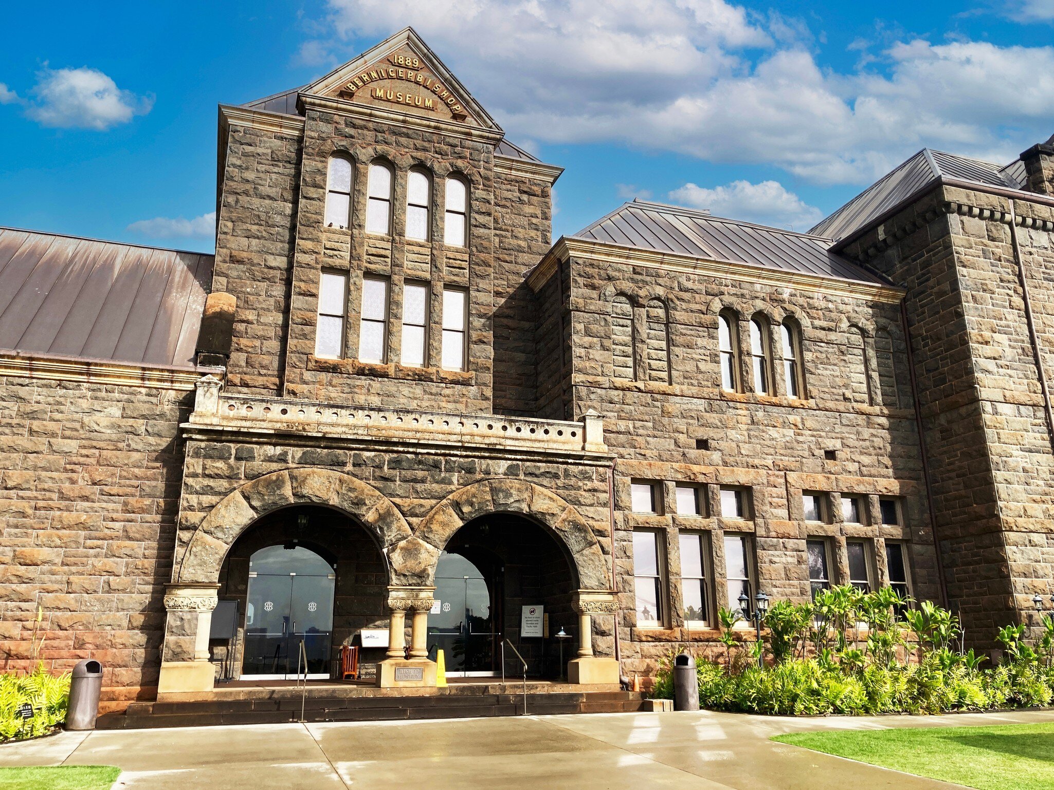 Grey stone facade with arched windows, twin entry arches and a gable inscribed Bernice P Bishop Museum