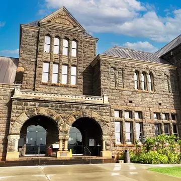 Grey stone facade with arched windows, twin entry arches and a gable inscribed Bernice P Bishop Museum