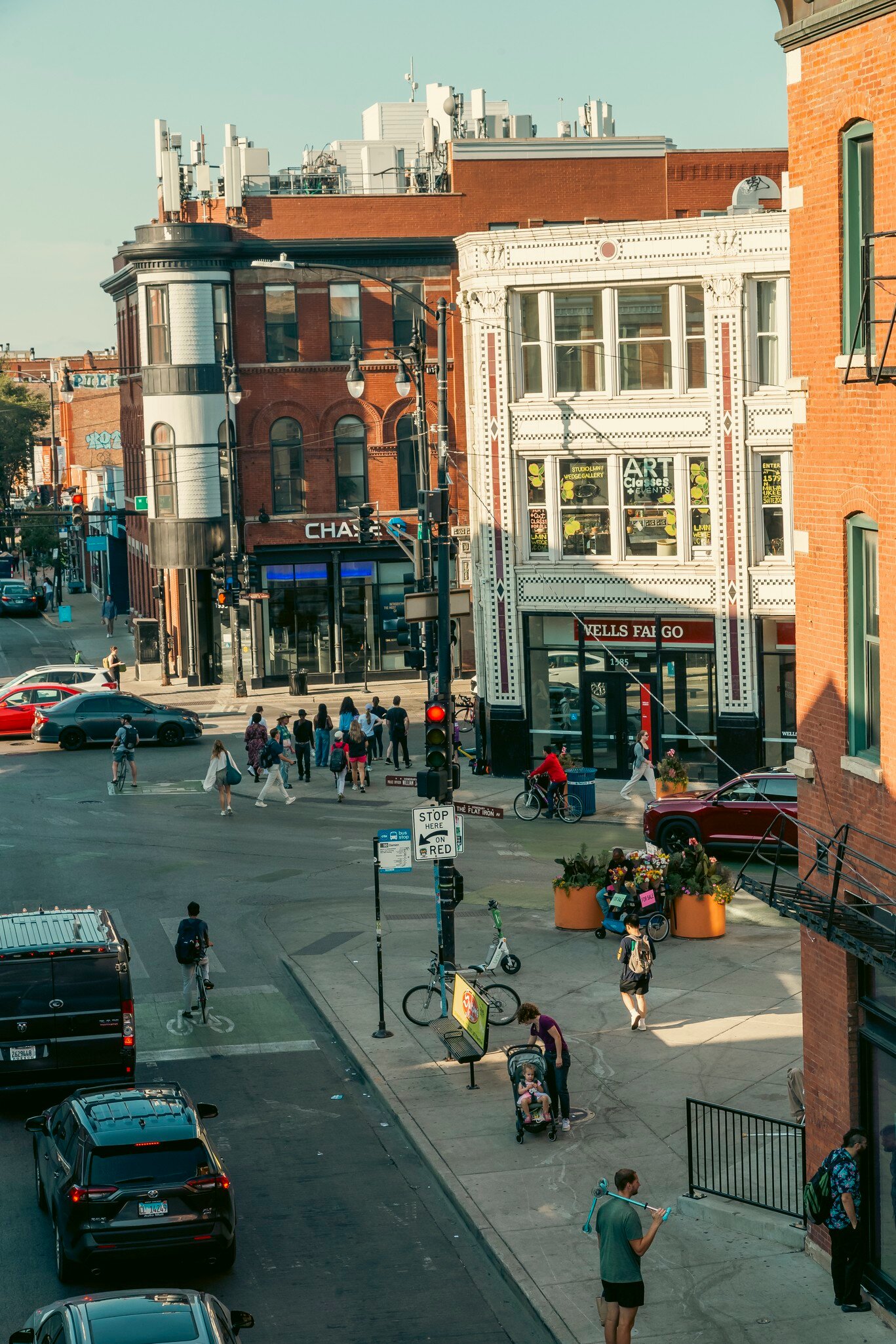 Street corner with crosswalks, cyclists and people walking past ornate brick and white-tiled buildings, Wicker Park, Chicago