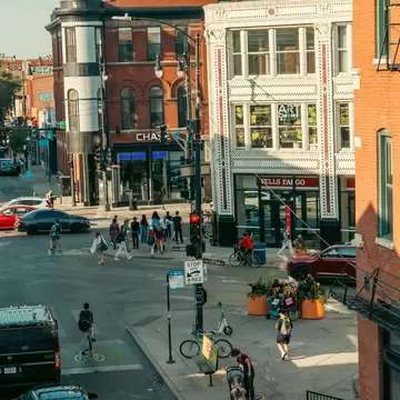 Street corner with crosswalks, cyclists and people walking past ornate brick and white-tiled buildings, Wicker Park, Chicago