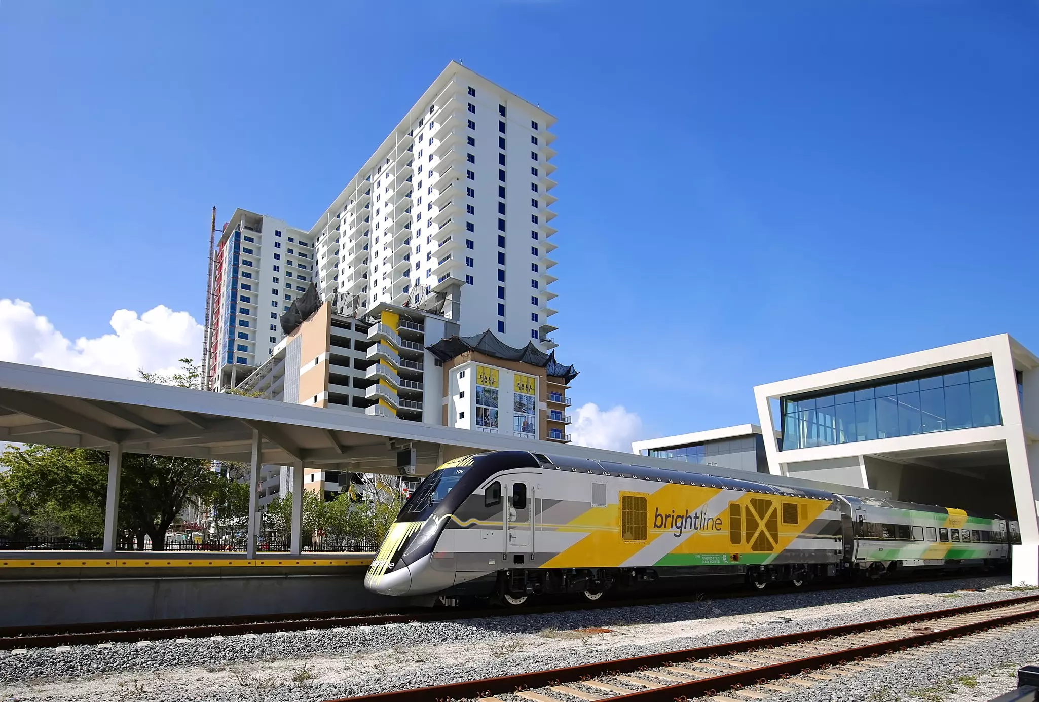 A sleek white, yellow and green passenger train goes by an aparment building that is under constuction