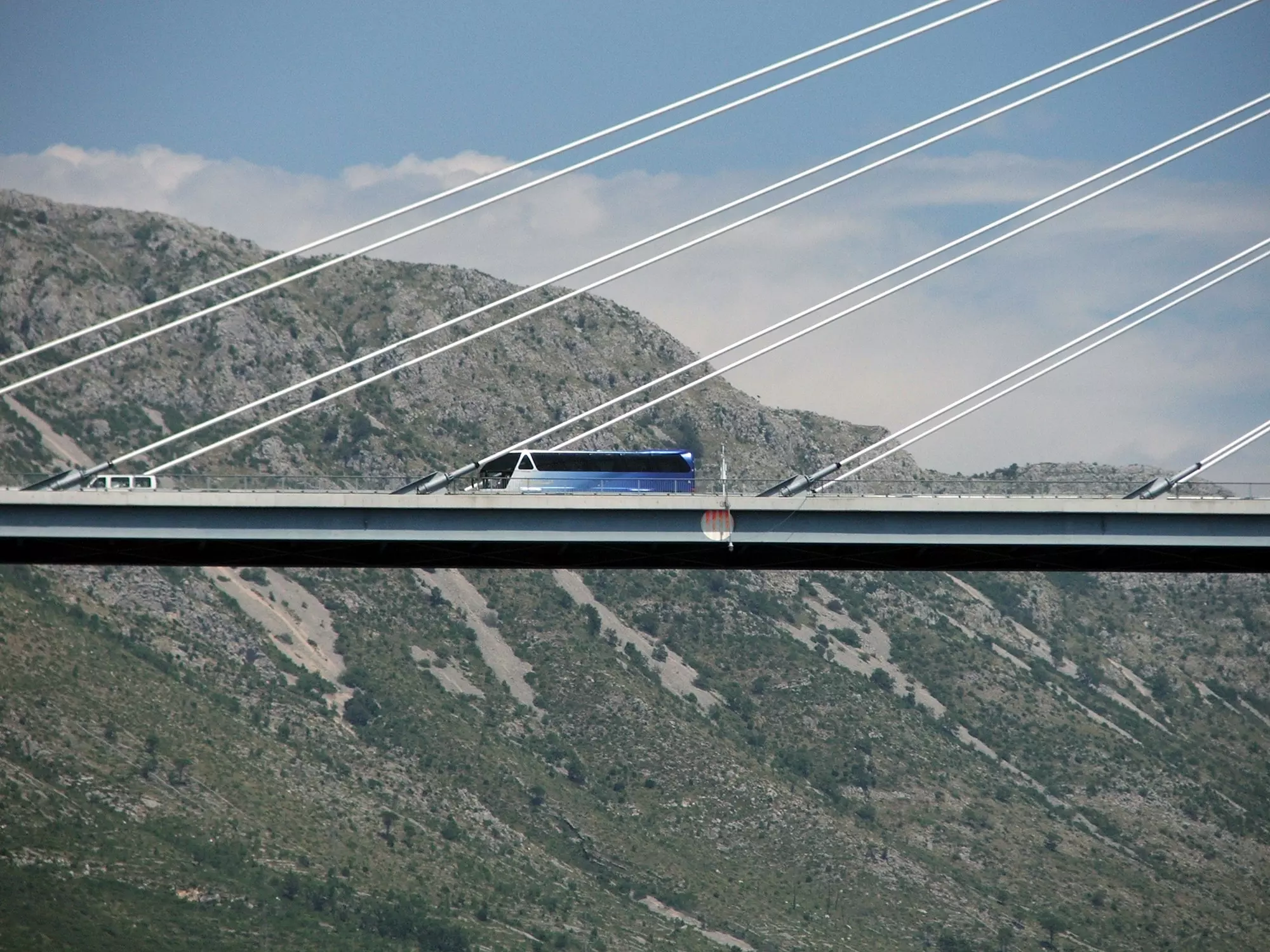 A close-up shot of a blue-painted coach on the span of a cable-stayed bridge over a rocky gorge.