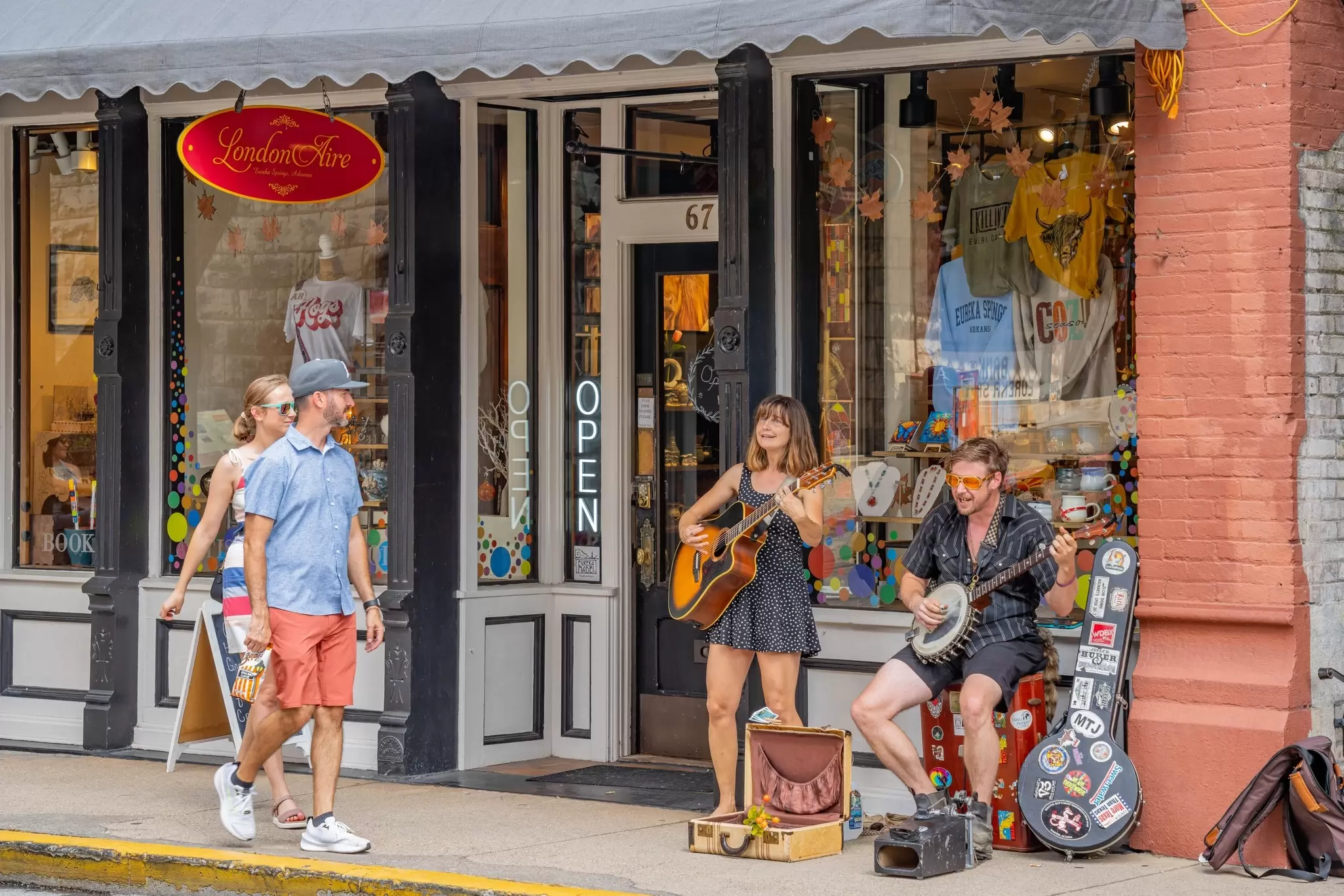 People walk past a storefront and musicians performing on the sidewalk in Eureka Springs, Arkansas, USA