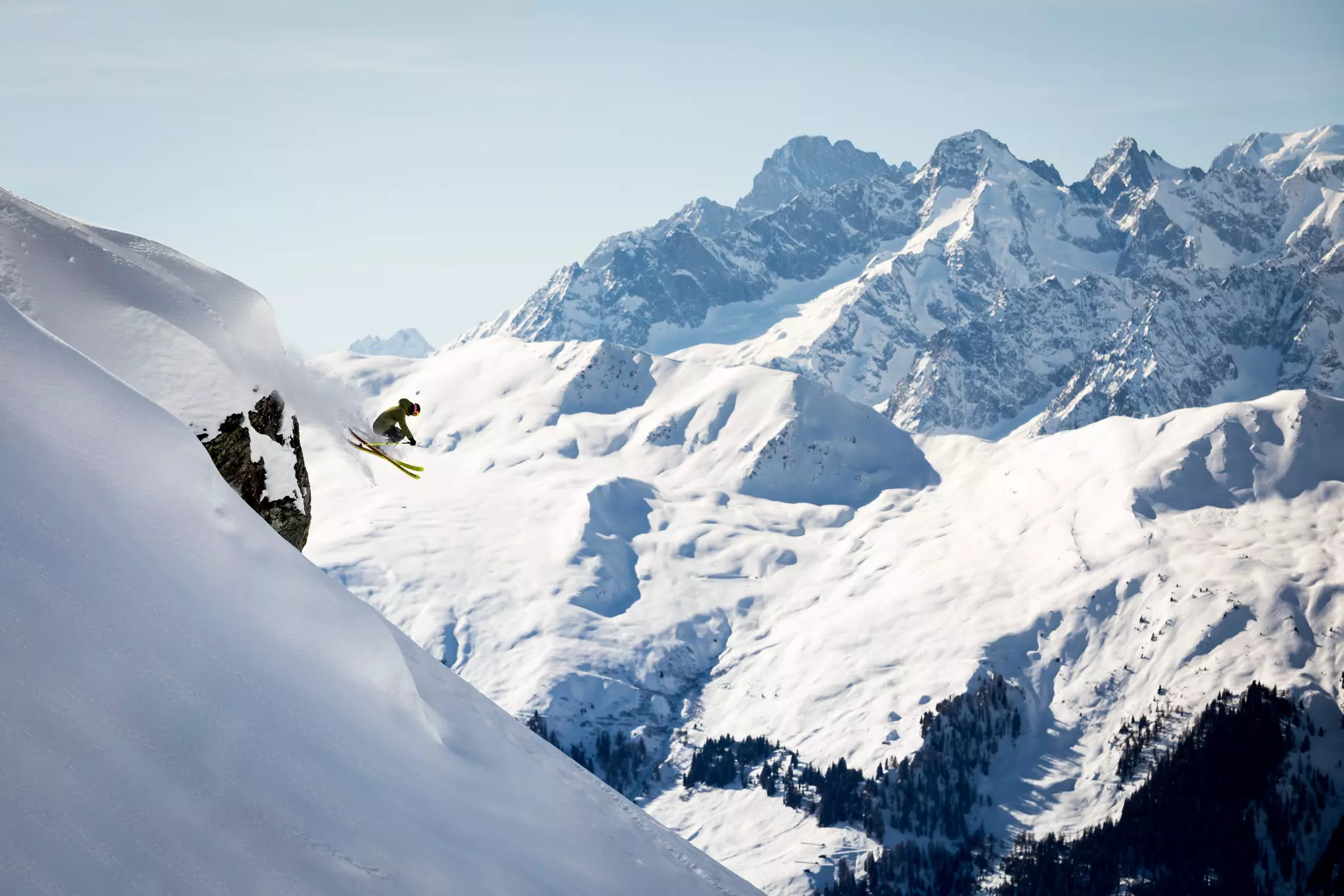 A skiier is airborne on a slope with snowy mountains in the background