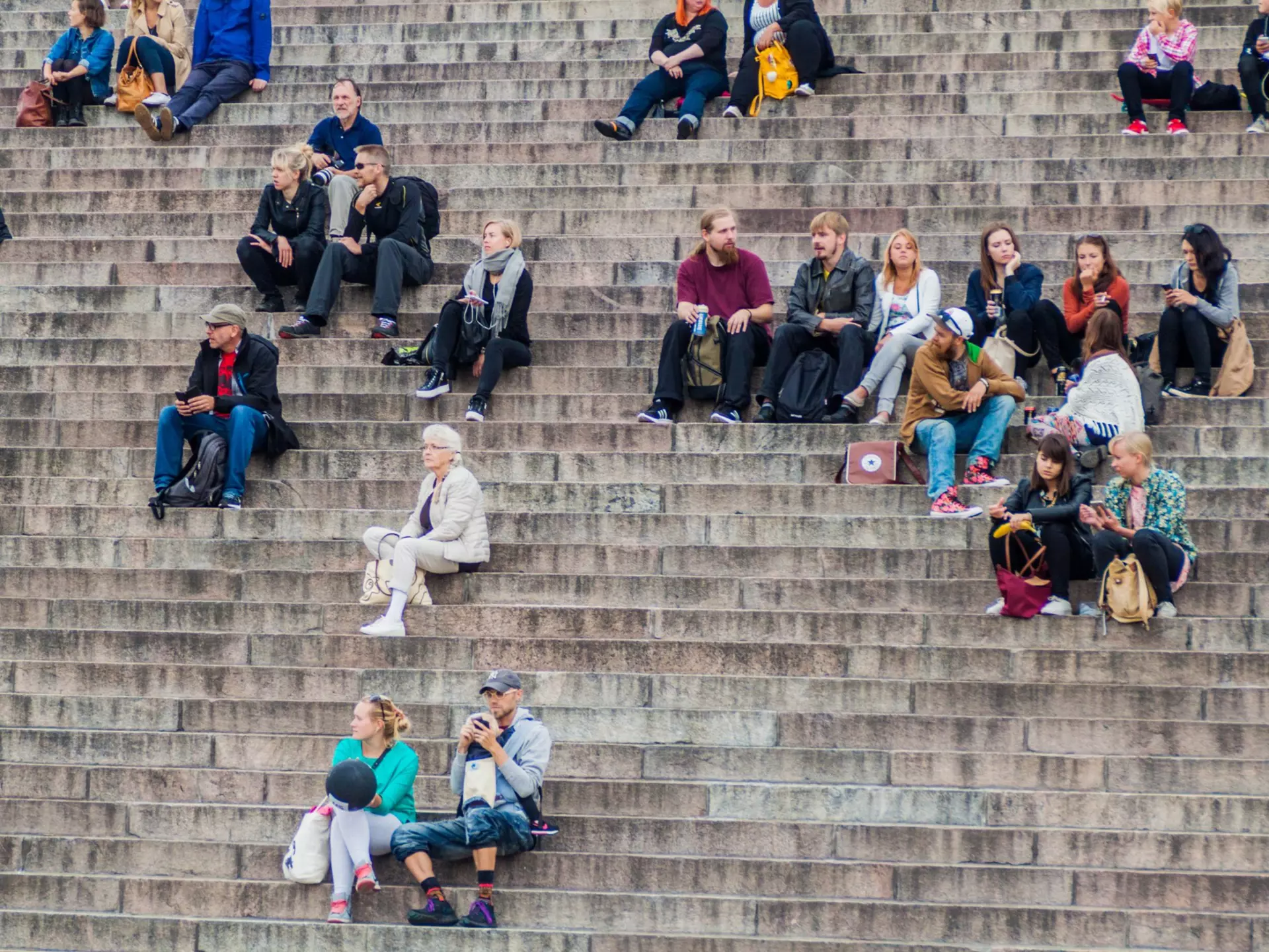 People sit on stairs on the Senate Square in front of the Finnish Evangelical Lutheran cathedral in Helsinki, FInland