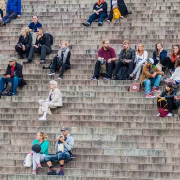 People sit on stairs on the Senate Square in front of the Finnish Evangelical Lutheran cathedral in Helsinki, FInland