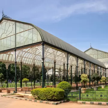 A long Victorian glasshouse of cast-iron columns and fanlight glazing, with clipped topiary and lawns around it under a hazy blue sky.