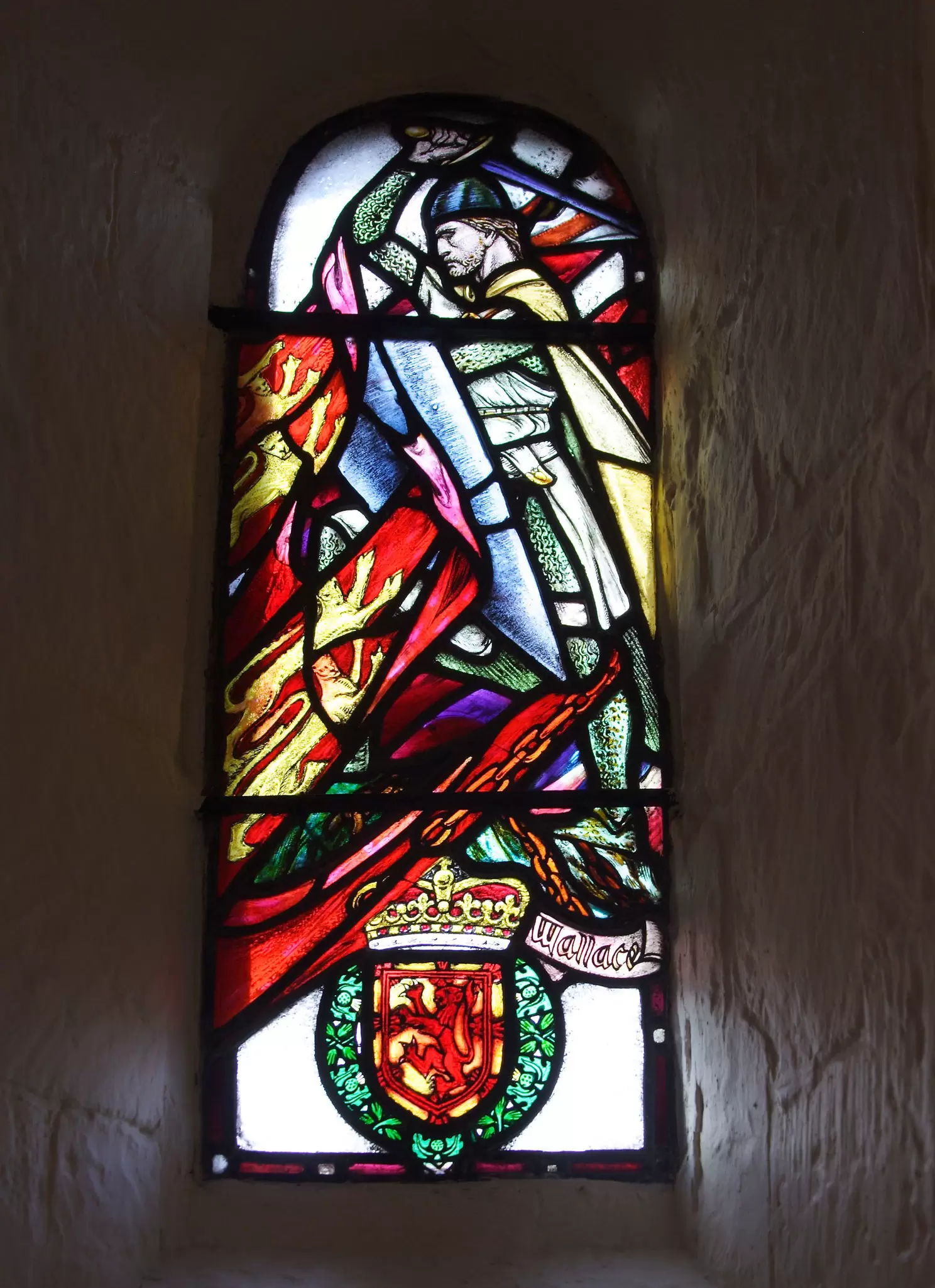 A stained glass window depicting a person in armour surrounded by colourful flags. There's a crest at the bottom