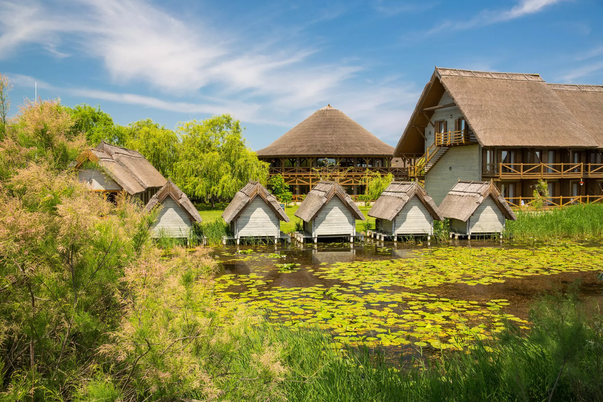 Traditional thatched-roof cottages are built along a waterway with leaves on the surface.