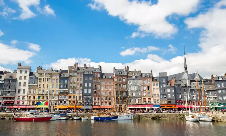 Narrow multistorey houses with café awnings line Honfleur's Vieux Bassin, sailboats moored on the still water
