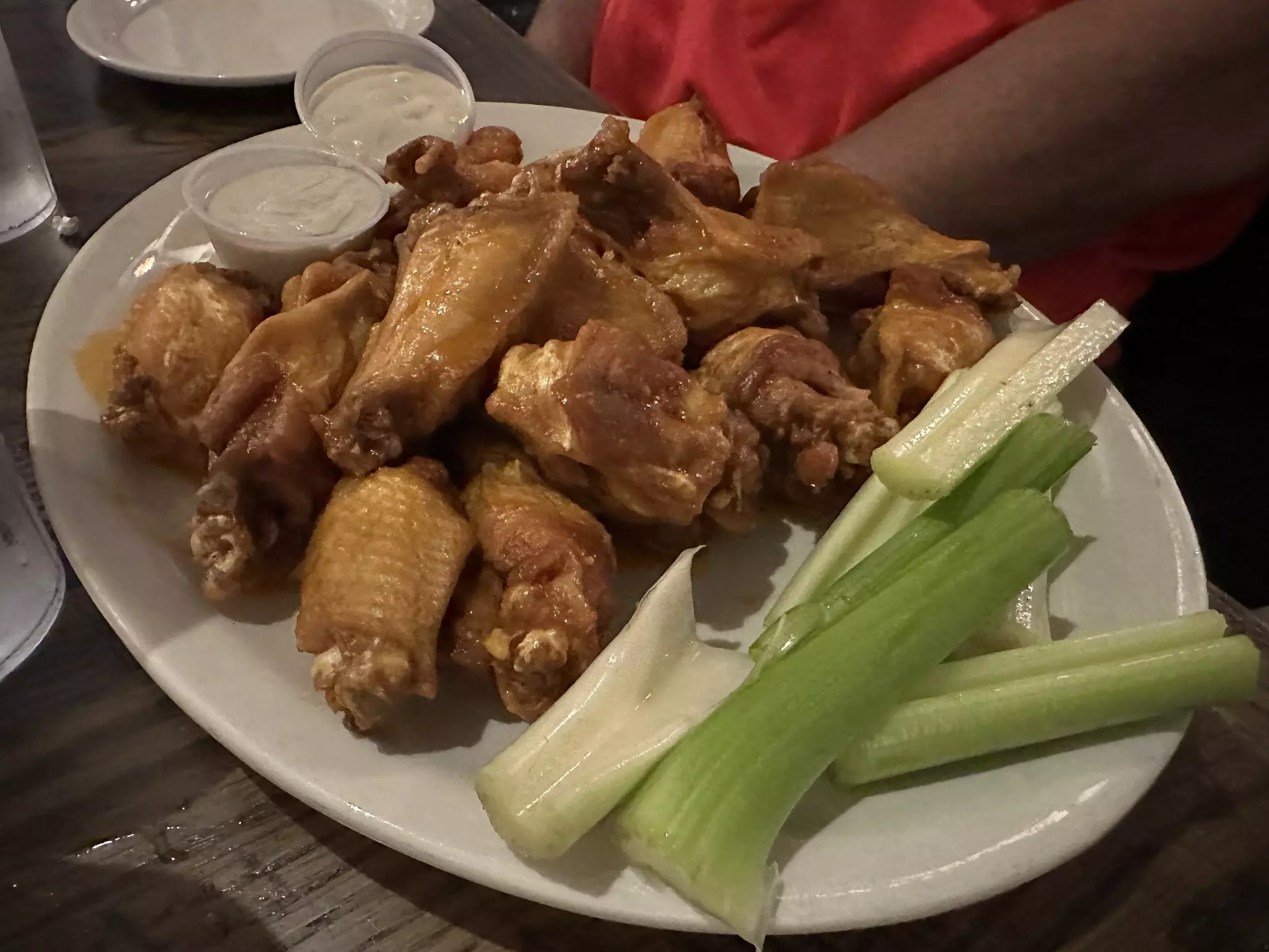 A dozen buffalo wings plated with celery and blue cheese dip.