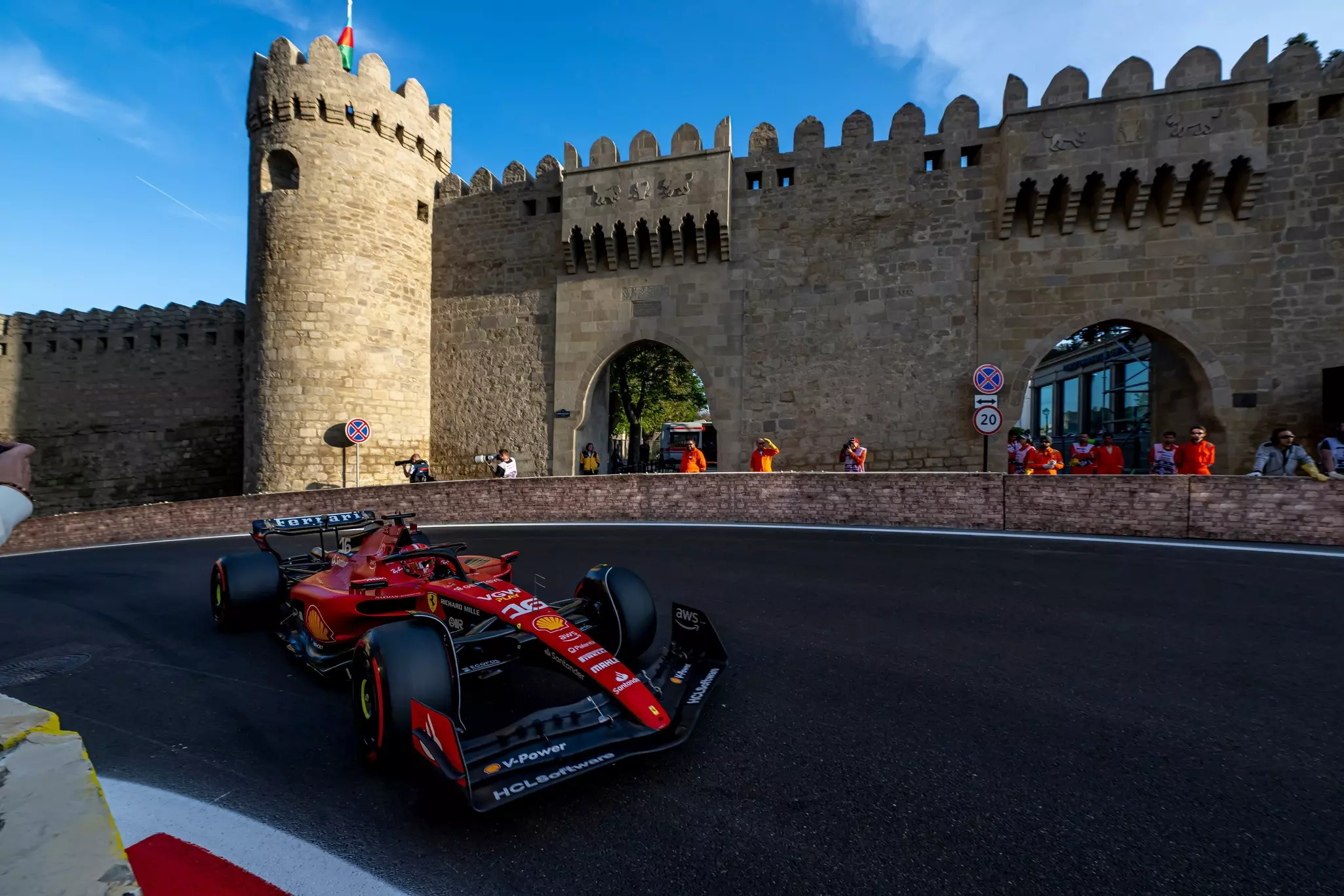 A red and black racing car comes round a bend near a grand fortress