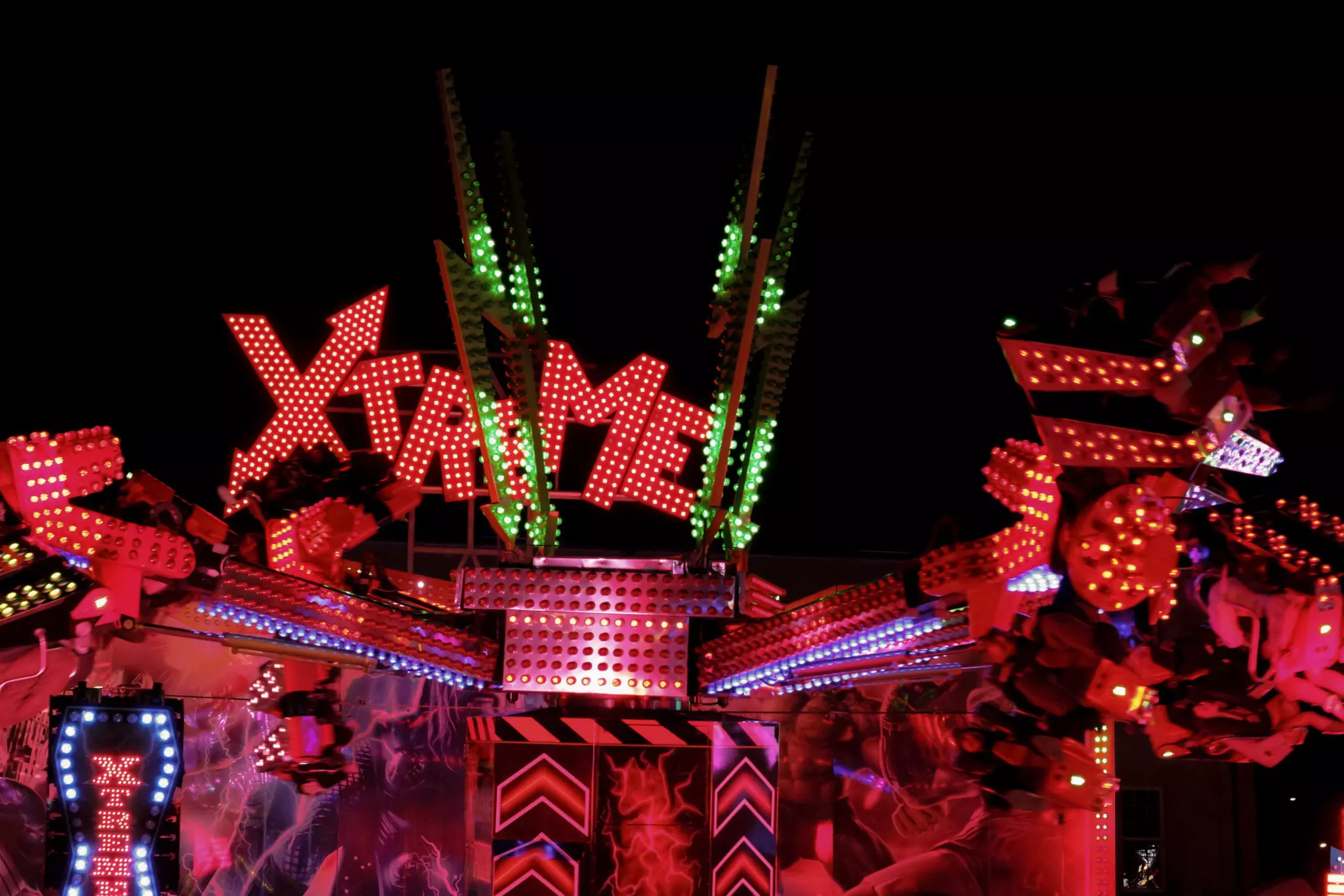 A theme park ride at night illuminated by colored lights.