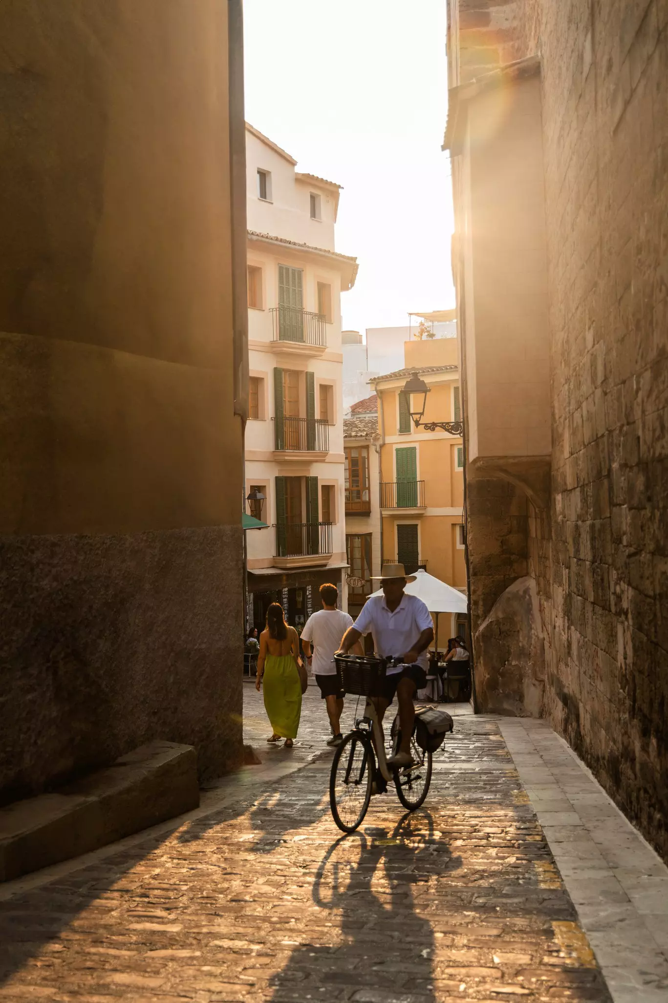 A man cycles through a narrow sunlit street in the old town of Palma de Mallorca.