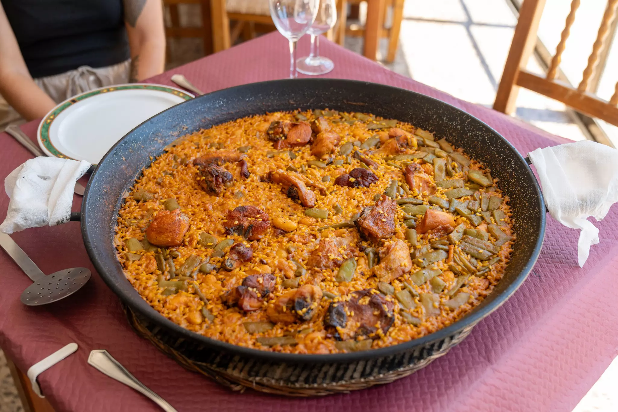 A paella dish with rabbit and vegetables is laid out on a table to share