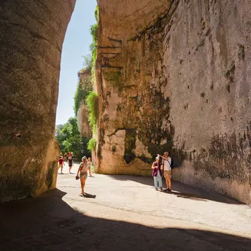 SIRACUSA, ITALY - JULY 18, 2019: Some tourists at the exit of the excavated cave, called Orecchio di Dioniso, near the Greek theater of Syracuse, in Sicily Italy., License Type: media, Download Time: 2025-12-10T16:35:55.000Z, User: sevelynd12, Editorial: true, purchase_order: 56500 - T&R or Kids, job: Global Publishing WIP, client: Dream Trips of Europe, other: Sharon / Dortenzio