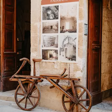 Museo Faggiano, Lecce: antique wooden bicycle against a limestone wall under a sign reading Museo Archeologico Faggiano