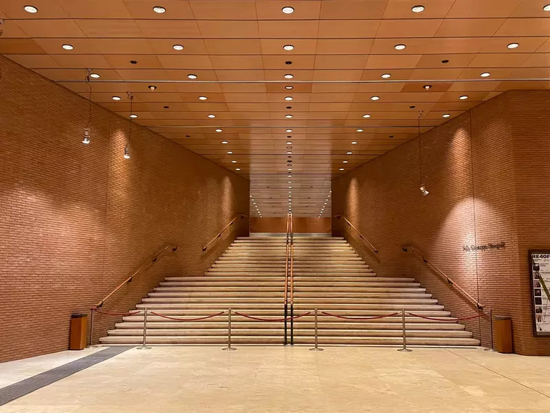 Tan bricks along a wide stairwell with a wood ceiling and copper railings