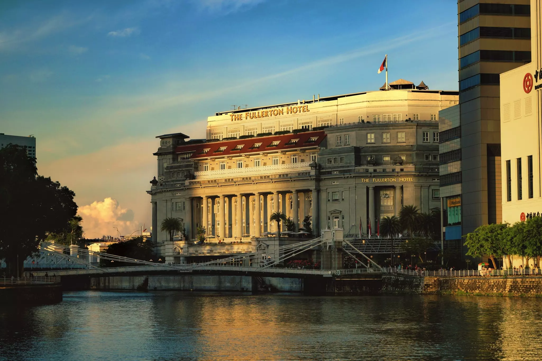A building across a body of water near a bridge; the facade is half in shadow, half in late afternoon sun.